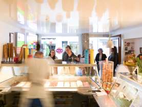 Eine Gelateria Theke mit einer grossen Auswahl an Gelatos. Gäste stehen vor der Theken an.