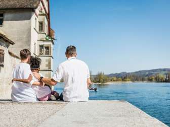 Familienausflug Stein am Rhein Mutter und Vater sitzen mit der Tochter auf einer Steinmauer am Rhein.