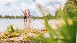 Zwei Personen stehen in Bademode im Rhein an einem Sandstrand.