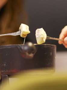 Zwei Personen essen Fondue und tunken gleichzeitig ihr Brot in den Käse.