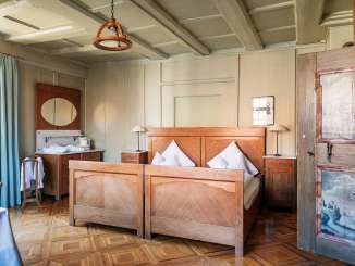 Gasthof Hirschen Stammheim Zimmer Ein Doppelholzbett mit weisser Bettwäsche. Ein alter filigraner Parkettboden. Die Wände sind Beige und die Holztüre hat landschaftliche Bemalungen.