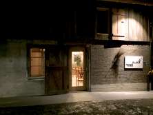 Die Fassade einer alten Scheune. Durch die Türe ist eine Bestuhlung zu sehen. Auf der rechten Seite des Eingangs ist ein Schild angebracht, wo "Hirschen Bühne" draufsteht.