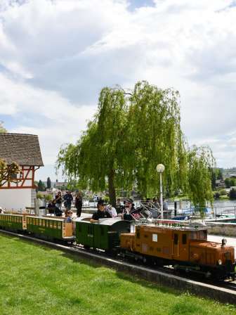 Liliputbahn Stein am Rhein Personen fahren mit einem Miniaturzug durch einen Park am Rhein.