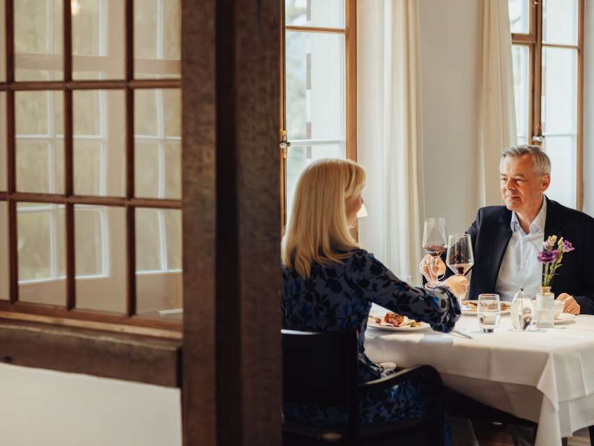 Festival gastronomique de Schaffhouse Un couple est assis à une table nappée de blanc. Ils ont un menu gastronomique devant eux et trinquent avec un verre de vin rouge.