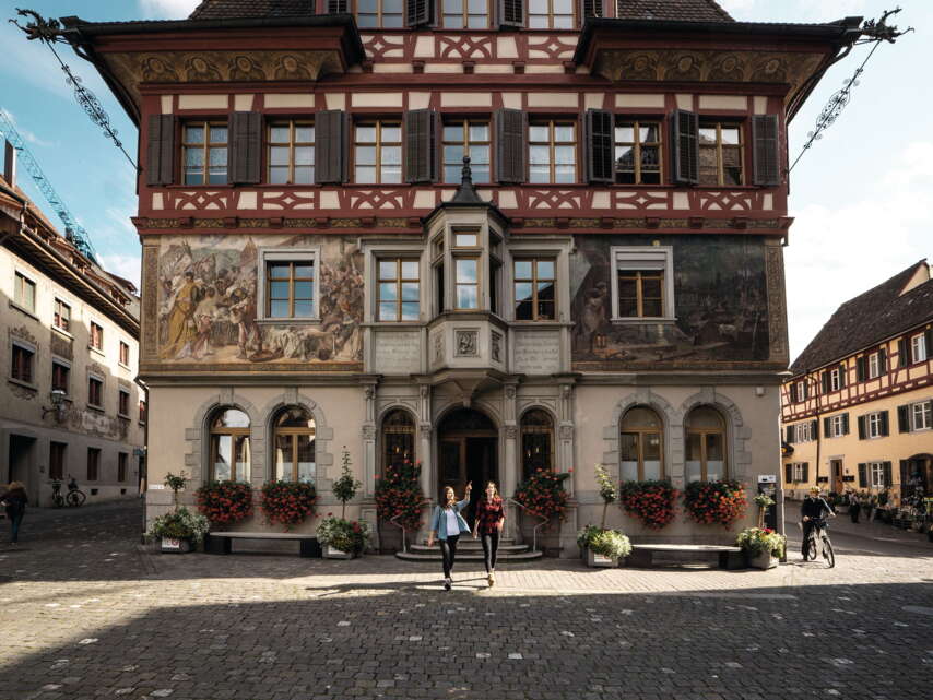 Zwei Wanderinnen stehen vor dem Rathaus in Stein am Rhein und starten ihre Wanderung.