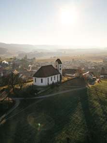 Wilchingen Dorf Auf einem Hügel mit Reben stehe eine Kirche. Dahinter sieht man das Dorf.