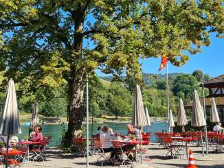 Terrasse Restaurant Unterhof Rote tische und Stühle sowie weisse Sonnenschirme stehen auf einer Terrasse direkt am Rhein.