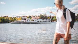 Eine Frau zeigt auf das Kursschiff, dass auf dem Rhein vorbei fährt.