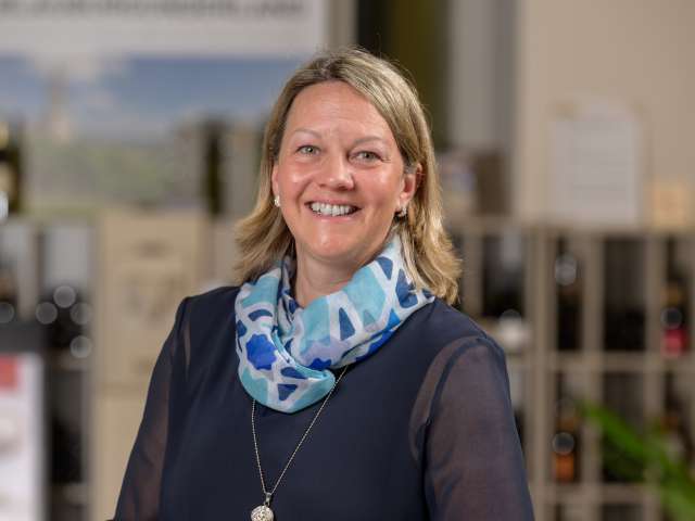 Portrait Kathrin Kuiper. Sie hat blonde Haare, trägt eine lange Kette, eine dunkelblaue Bluse und eine blaues Foulard.