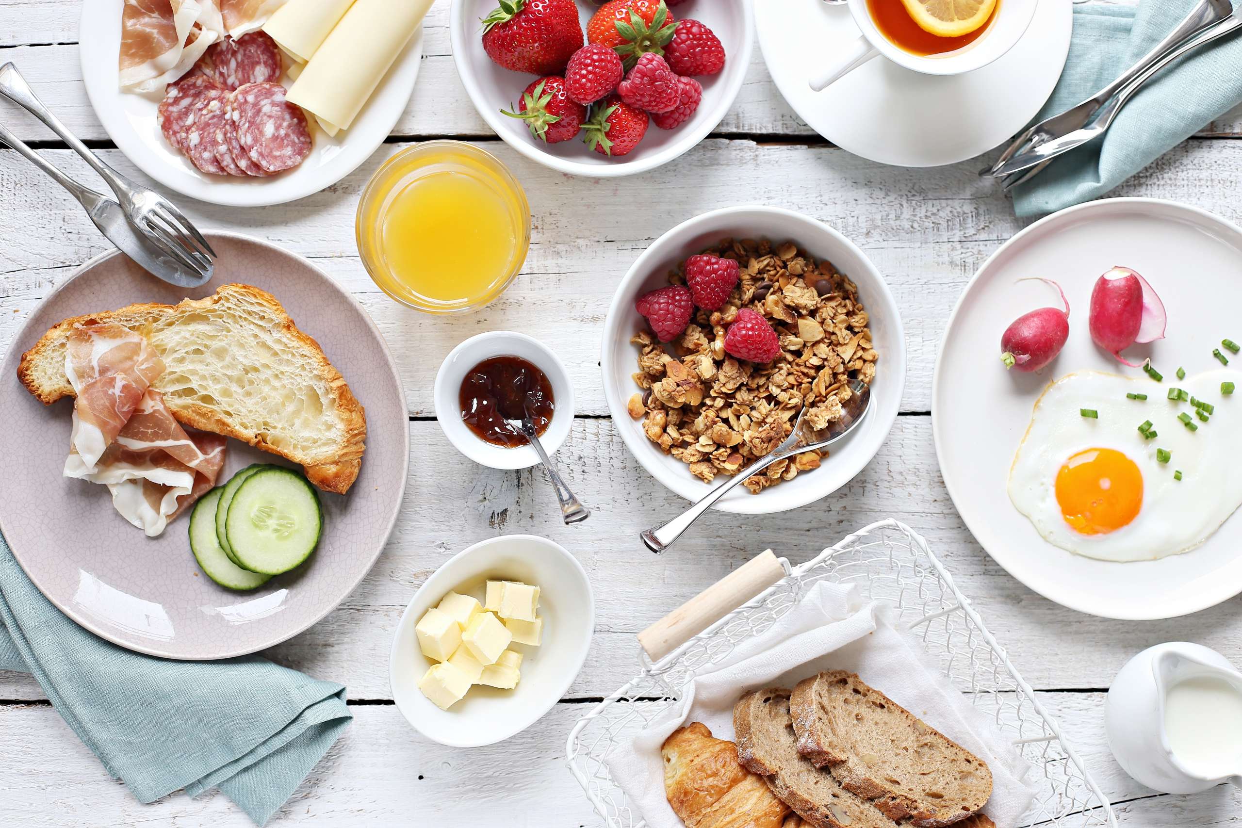 Holztisch mit Müesli, Brot, Aufschnitt, Spiegelei und Beeren.