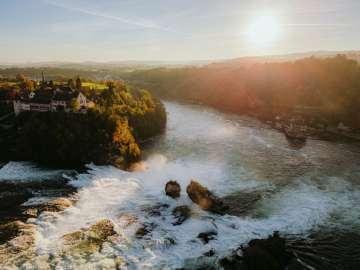 Rheinfall Herbst Blick von oben auf die Beiden Felssen im Wasserfall, links das Schloss Laufen und rechts das Schlössli Wörth. Goldenes Abendherbstlicht scheint auf den Wasserfall.