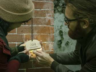 Sato-Kodex Zwei Personen versuchen draussen auf einem Escape Room ein spezielles Schloss zu knacken.