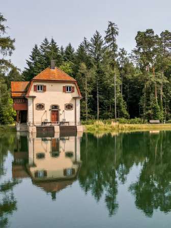 Engeweiher Schaffhausen Ein Weiher mit blau grünem Wasser ist umgeben von Wald. Am Ufer steht ein kleines Häuschen.