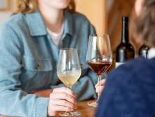 Zwei Freudinnen sitzen an einem Holztisch. Eine Frau hat ein Glas Weisswein und die andere ein Glas Rotwein in der Hand.
