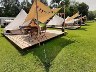 Glamping Freizeitanlage Rheinwiese Drei Glampingzelte auf einer Holzplattform. Vor dem Zelteingang hat es ein Vordach sowie ein Tisch mit vier Stühlen.