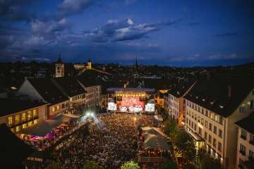 Ein Platz zwischen Häuser in der Altstadt. Der Platz ist gefüllt mit Menschen. Vorne Befindet sich eine Bühne mit der Aufschrift "Stars in Town".