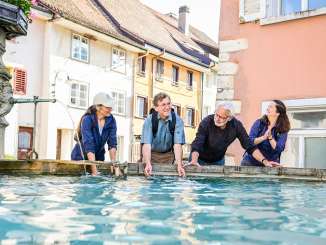 Vier Personen stehen an einem Brunnen im Städtchen Neunkirch und kühlen die Arme im Wasser ab.