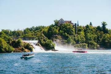 Ein blaues und ein pinkes Boot fahren im Rheinfallbecken vor dem grössten Wasserfall Europas.