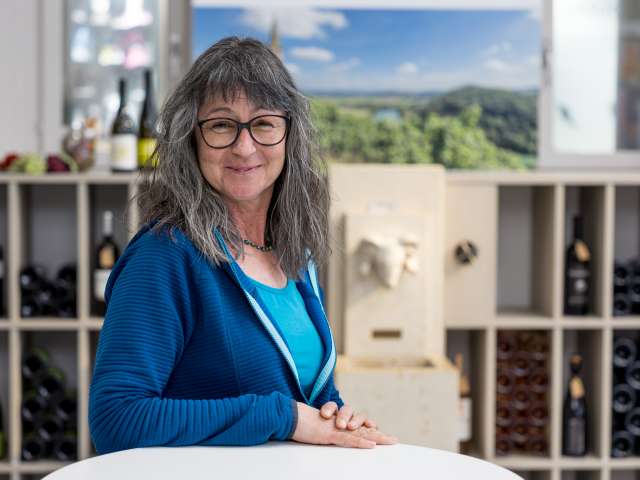 Portrait Andrea Kummer. Sie trägt ein hellblaues T-Shirt und eine dunkelblaue Jacke. Sie trägt eine Kette und Brille.