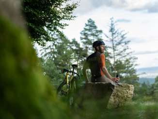 Ein Velofahrer sitzt auf einem grossen Stein und macht eine Pause auf seiner Graveltour.
