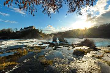 Blick auf den Rheinfall von Hinten mit dem Schloss Laufen im Hintergrund. Der Rheinfall wurde im Winter gegen die Sonne fotografiert.