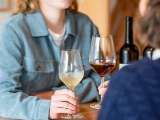 Weindegu Leibacher Stein am Rhein Zwei Freudinnen sitzen an einem Holztisch. Eine Frau hat ein Glas Weisswein und die andere ein Glas Rotwein in der Hand.