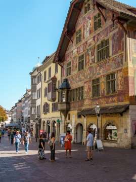 Stadtführung Schaffhausen Eine Gruppe mit Guide steht vor einem Haus reichlich verziert mit Fassadenmalereien und einem Erker.
