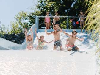 KSS Freizeitpark Schaffhausen Vier Kinder rutschen in einem Freibad gemeinsam eine breite Rutschbahn hinunter.