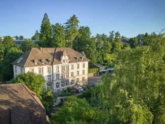 Blick auf ein stattliches Haus umgeben von Bäumen und Natur.