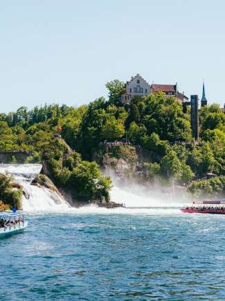Ein blaues und ein pinkes Boot fahren im Rheinfallbecken vor dem grössten Wasserfall Europas.