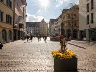 Warm eingekleidete Personen laufen bei Sonnenschein über den Fronwagplatz.
