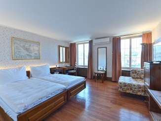 Doppelzimmer Hotel Rheinfels Doppelzimmer Hotel Rheinfels. Auf einem dunklen Holzboden steht ein Doppelbett mit weisser Bettwäsche. Die Wände sind mit blumigen Tapeten verkleidet.