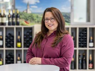 Portrait Tanja Hürlimann. Sie trägt eine burgund farbige Bluse. Sie hat länge braune Haare und trägt eine Birlle.