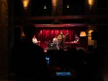 Eine vierköpfige Band. Die Leadsängerin steht mit einer Gitarre. Das Mischpult ist im Vordergrund in der Mitte des Bildes.