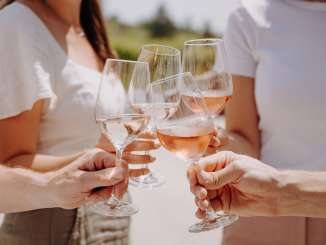 Vier Personen stossen mit einem Glas Wein ein. Es sind zwei Weissweine und zwei Rosé.