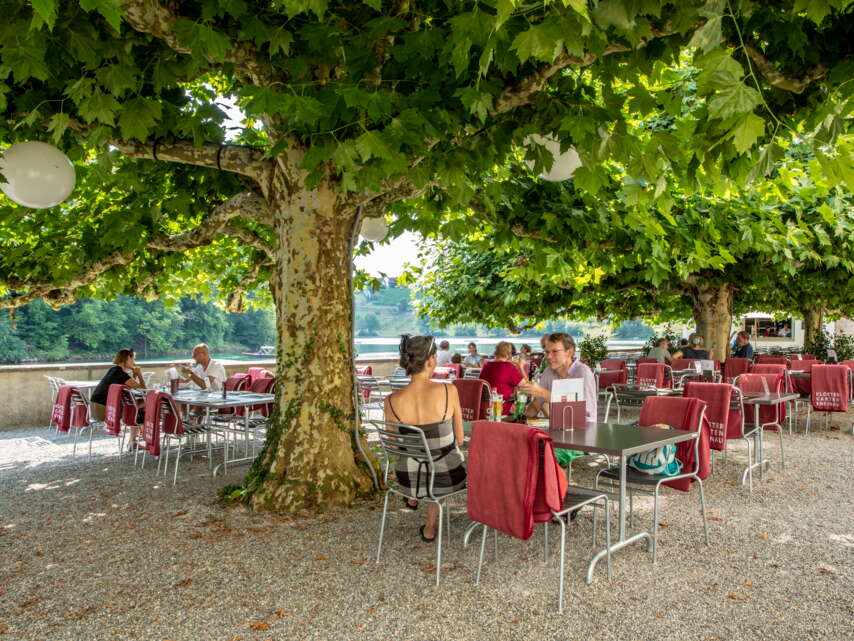 Gartenwirtschaft direkt am Rhein und unter Bäumen des Restaurant Klostergarten in Rheinau. Über den Stühlen hängen rote Wolldecken.