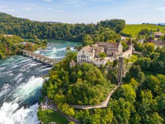 Blick von oben auf ein von grün umgebenes Schloss direkt am Rhein und Rheinfall.