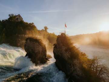 Rheinfall im Herbst Blick von hinten auf die zwei Felsen mitten im Wasserfall. Goldies Licht scheint auf den Wasserfall.