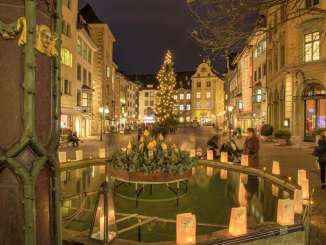 Weihnachtsbeleuchtung auf dem Fronwagplatz in der Schaffhauser Altstadt. In der Mitte steht ein Tannenbaum mit einer Lichterkette und auf dem Mohrenbrunnen stehen Teelichter