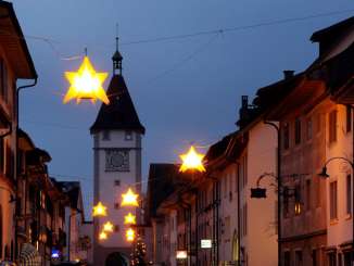 Leuchtende Sterne hängen über einer Gasse in Neunkirch. Im Hintergrund sieht man einen Turm.