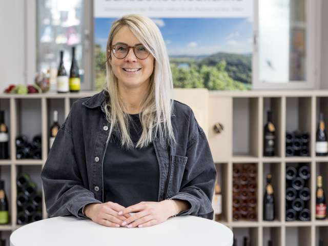 Portrait Corinne Müller. Sie hat sehr helle blonde lange Haare, trägt eine Brille, ein schwarzer T-Shirt und eine schwarze Jacke.