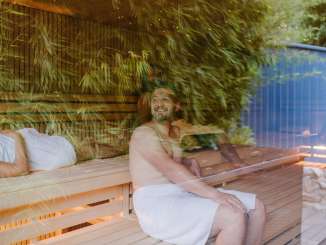 Personen sitzen in einer Sauna. Im Glas spiegeln sich Bambusblätter.