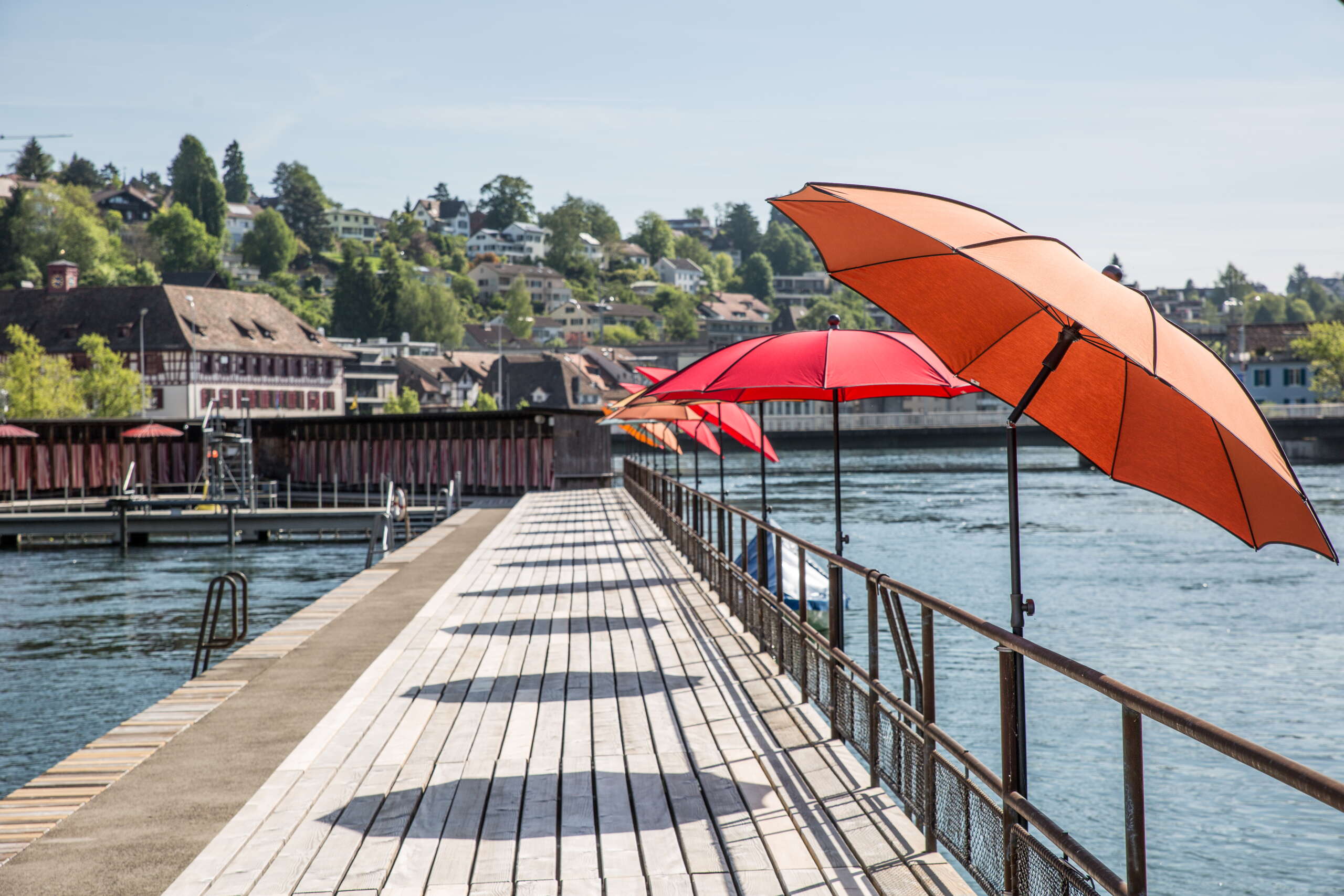 Kastenbad direkt im Rhein mit roten Sonnenschirmen. Im Spitz des Kastenbades sind Umkleidekabinen mit rot weiss gestreiften Vorhängen.