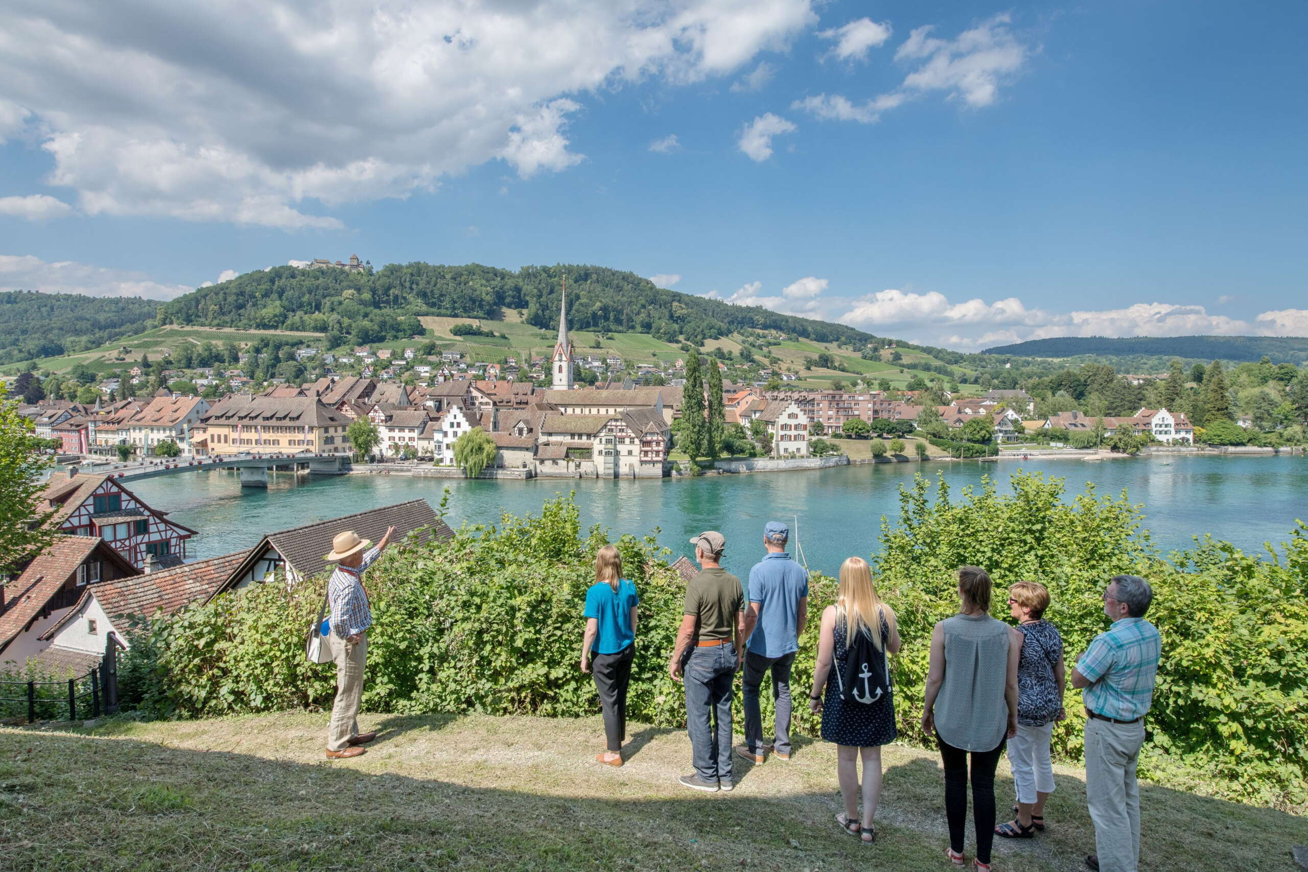 Gruppe der Stadtführung Stein am Rhein steht auf der anderen Rheinseite mit Stein am Rhein im Hintergrund