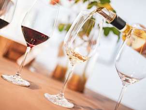 Weindegustation Es stehen vier Weingläser auf einem Tisch. Zwei davon sind mit Rotwein befüllt, eines ist Leer und in einem wird Weisswein eingeschenkt.