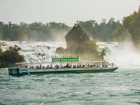 Ein grünes Schiff gefüllt mit Personen. Auf dem Schild auf dem Dach des Schiffes steht: 30 min Rundfahrt. Ebenfalls ist das Schiff mit www.schiffmaendli.ch angeschrieben. Im Hintergrund ist ein Felsen zu sehen.