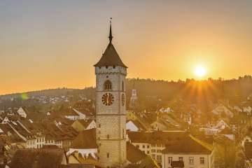 Die goldene Abendsonnen leuchtet auf die Schaffhauser Altstadt. Im Vordergrund ragt der Kirchenturm des St. Johanns über die Hausdächer.