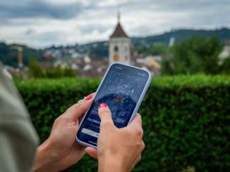 Eine Hand hält ein Handy. Darauf sieht man das digitale Rätsel Foxtrail GO.