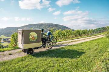 Velosafari Schaffhauserland Zwei Freudinnen sind mit den E-Bike in den Reben unterwegs. Bei einem Cargovelo hat es einen ausklappbaren Zeltaufbau.