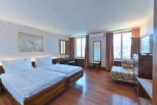 Doppelzimmer Hotel Rheinfels. Auf einem dunklen Holzboden steht ein Doppelbett mit weisser Bettwäsche. Die Wände sind mit blumigen Tapeten verkleidet.